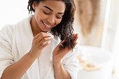 African American Woman Applying Serum On Damaged Hair In Bathroom