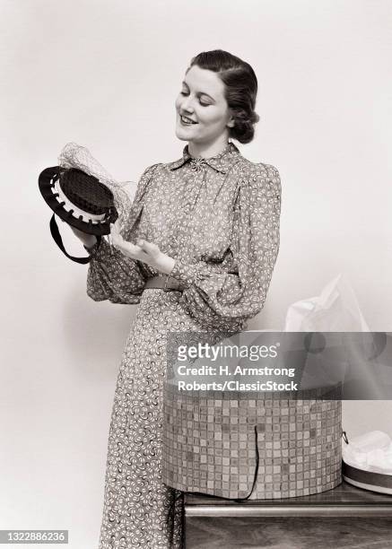 1940s Smiling Brunette Woman In Print Dress Admiring A New Hat Jt Taken Out Of A Hatbox.