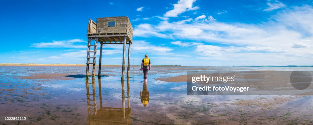 Woman walking over tidal beach Lindisfarne Pilgrims Way panorama Northumberland