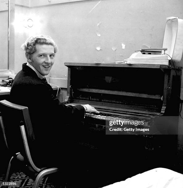 American "rock n'' roll" singer and pianist Jerry Lee Lewis smiles over his shoulder while playing the piano in a dressing room in an undated photo....