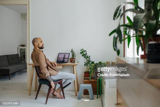 hombre sentado en casa y navegando por destinos de viaje en su computadora portátil - adaptable fotografías e imágenes de stock