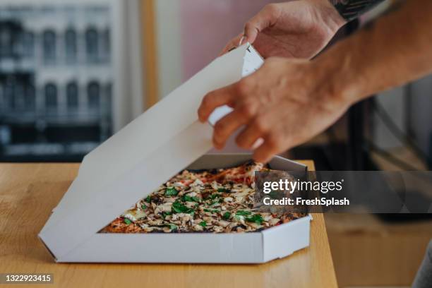 anonymer student öffnet eine kiste pizza, die er während seiner studienpause essen wird - pizza delivery stock-fotos und bilder