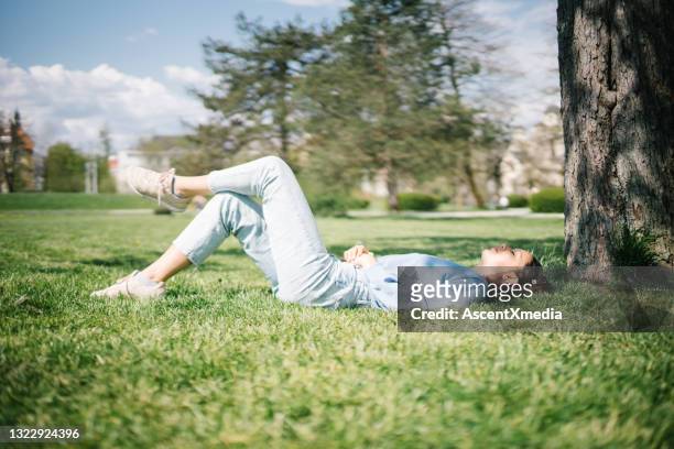 junge frau entspannt sich im sonnigen stadtpark - hände auf bauch stock-fotos und bilder