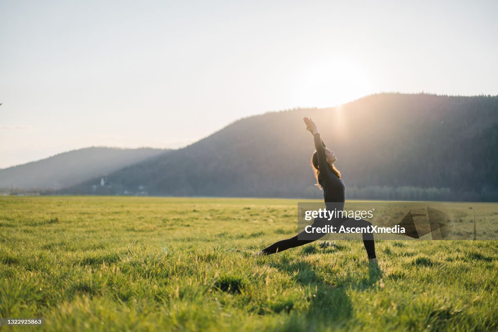 Young woman practices yoga in grassy meadow at sunrise