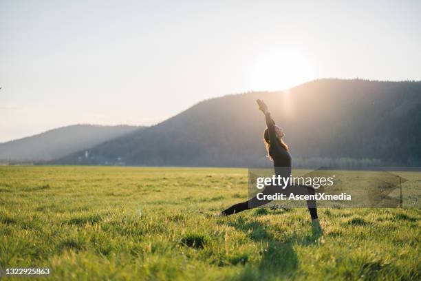 young woman practices yoga in grassy meadow at sunrise - ioga imagens e fotografias de stock