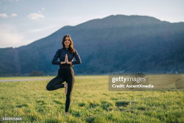 de jonge vrouw oefent yoga in grasrijke weide bij zonsopgang uit - op een been staan stockfoto's en -beelden