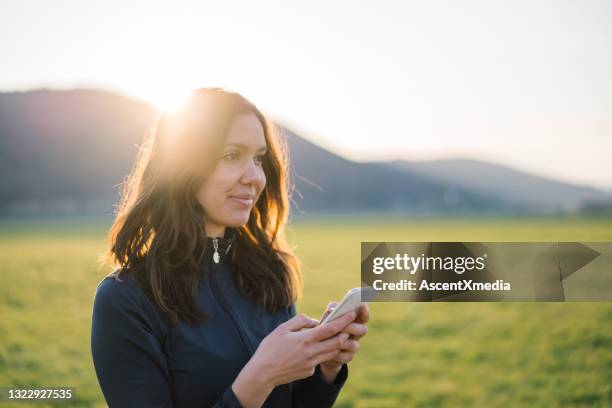 female trail runner texts on cellphone in grassy meadow - see far stock pictures, royalty-free photos & images