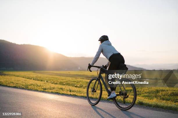 young woman bikes down country road at sunrise - bike riding stock pictures, royalty-free photos & images