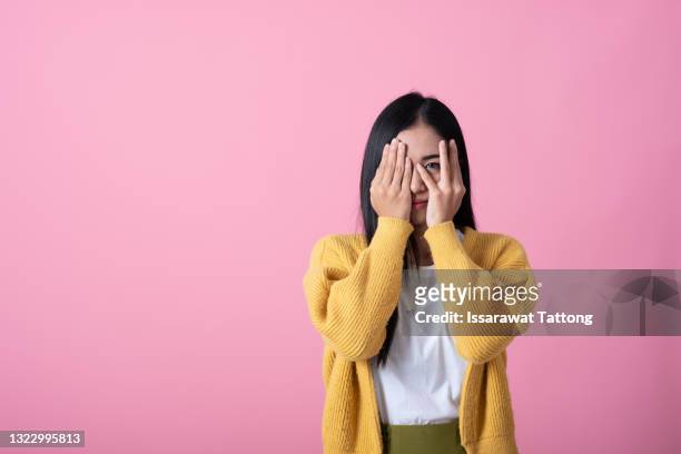 a picture of a scared woman covering her eyes over pink background - shy foto e immagini stock