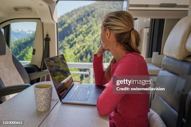 young woman in her camper van works on laptop - camper van imagens e fotografias de stock