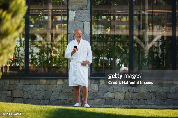senior man standing outdoors on terrace of wellnest resort, relaxing. - robe stock pictures, royalty-free photos & images