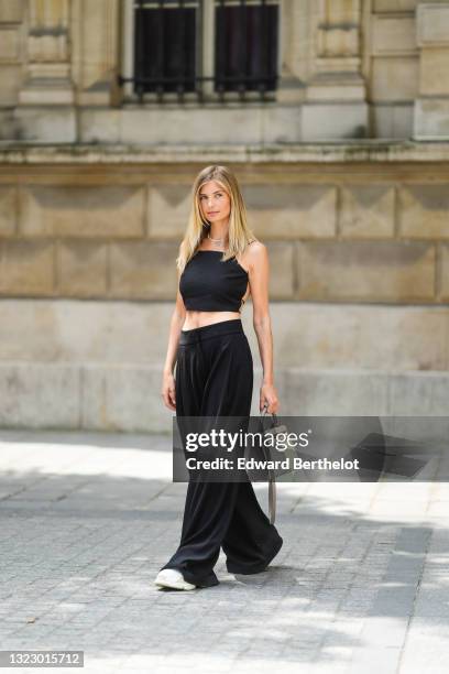 Xenia Adonts wears a beaded necklace with a mini blue teddy bear, a black back-nude sleeveless off-shoulder cropped tank top from Paloma, wide leg...