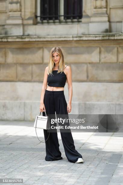 Xenia Adonts wears a beaded necklace with a mini blue teddy bear, a black back-nude sleeveless off-shoulder cropped tank top from Paloma, wide leg...