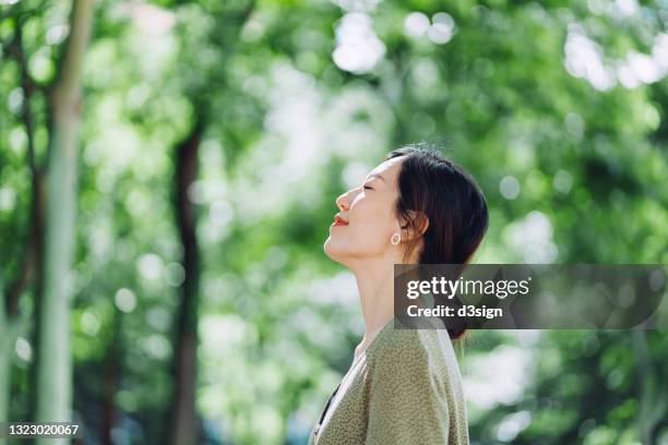 beautiful young asian woman meditating in the nature with her eyes closed, setting herself free and feeling relieved. enjoying fresh air and breathing in the calmness with head up against sunlight in the morning. freedom in nature. connection with nature - one young woman only health hopeful stock pictures, royalty-free photos & images