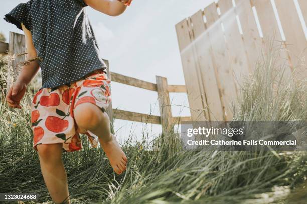 child surrounded by fences, runs on grass in low sun - running in the sun stock-fotos und bilder