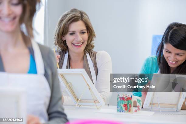 two friends enjoying themselves while they paint during an art class - art class stock pictures, royalty-free photos & images