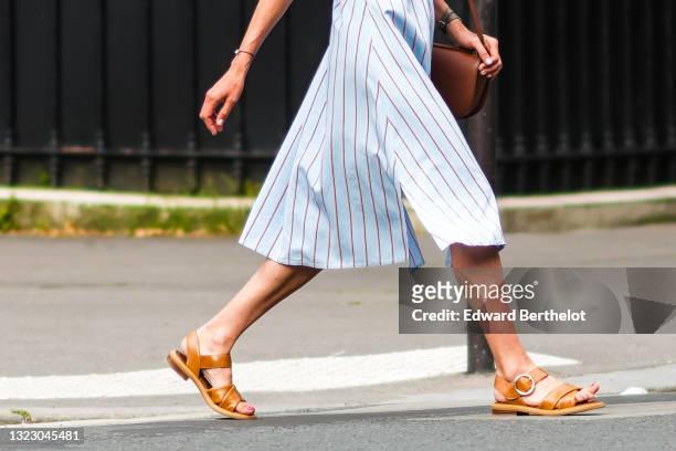 Passerby wears a pale blue with brown stripes shirt knees dress, a brown shiny leather shoulder bag, a brown leather bracelet, a black bracelet,...