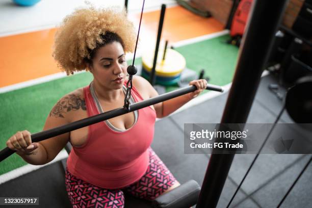 jovem puxando máquina de peso na academia - mulher gorda - fotografias e filmes do acervo