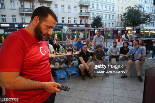Turkish team fan adjusts a television set outside a late-night shop on the sidewalk while watching the EURO 2020 kick-off Turkey v Italy match on...