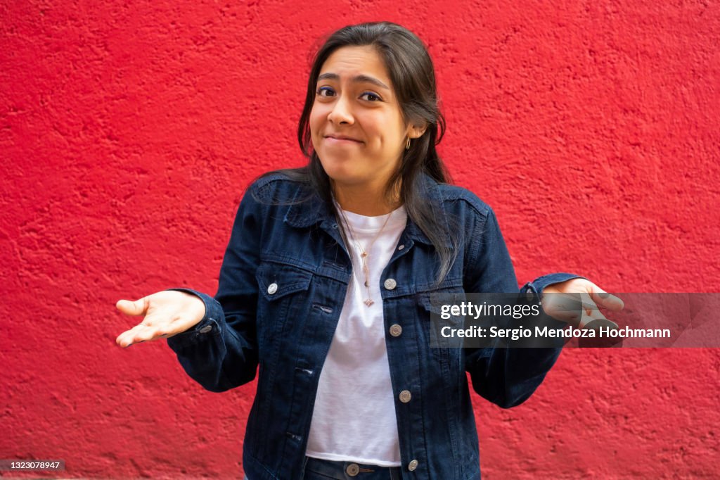 Young Latino woman shrugging with her hands to her sides, red background