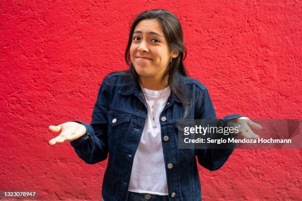 young latino woman shrugging with her hands to her sides, red background - förnekande bildbanksfoton och bilder