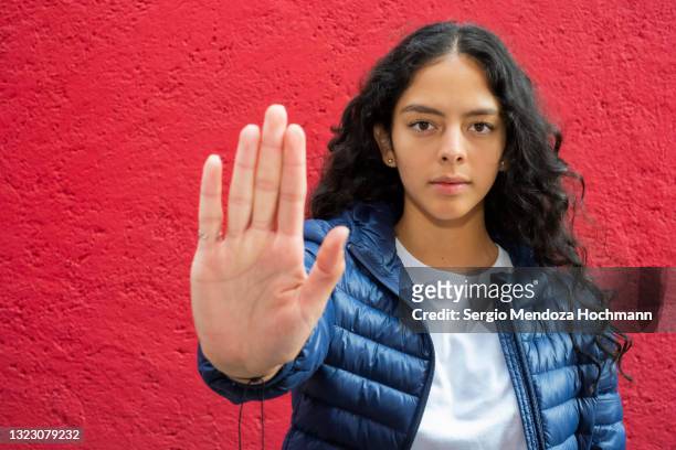 young latino woman looking at the camera and gesturing to stop, red background - raped women fotografías e imágenes de stock