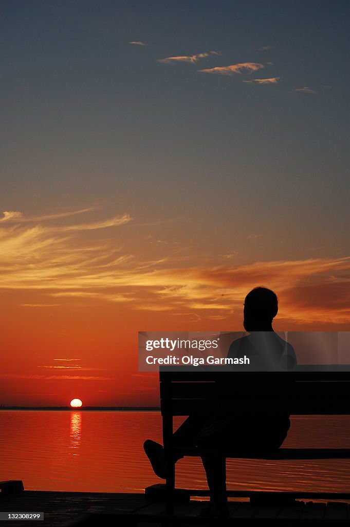 Man watching sunrise on bench by beach