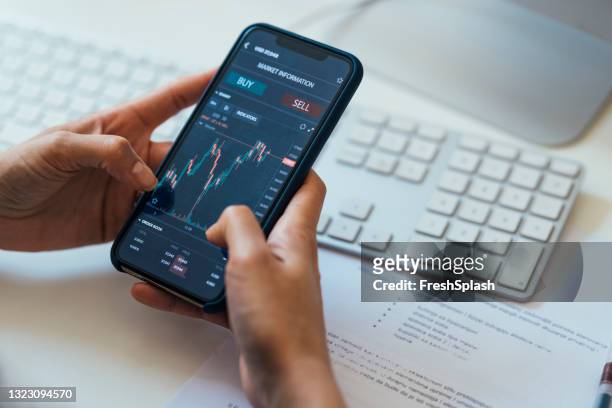 nahaufnahme einer anonymen frau, die ein smartphone mit einem börsendiagramm auf dem bildschirm hält - stock market and exchange stock-fotos und bilder