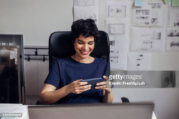 smiling businesswoman making a break from work to check messages on her smartphone - games workshop stock pictures, royalty-free photos & images