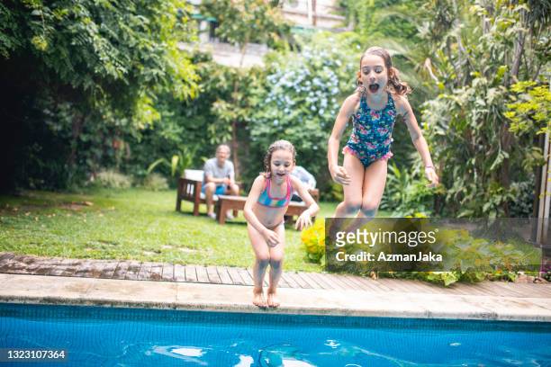 unbekümmerte junge schwestern springen ins schwimmbad - family playing in backyard pool stock-fotos und bilder