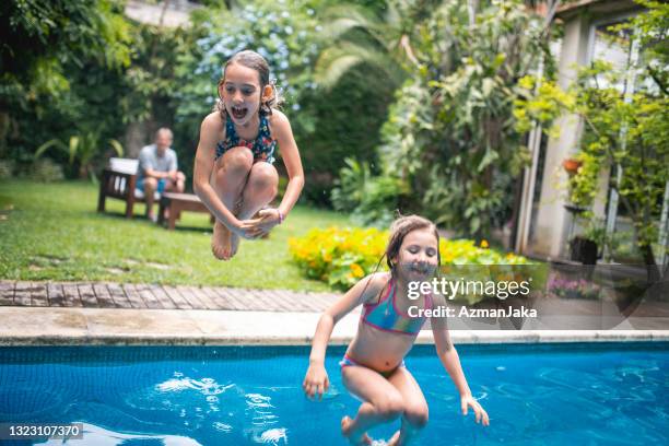 fun sisters jumping into family swimming pool - young girl jumping into swimming pool stock pictures, royalty-free photos & images