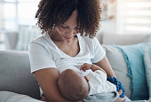 Shot of a young woman breastfeeding her adorable baby girl on the sofa at home