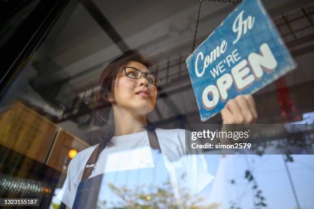 gelukkige aziatische bedrijfseigenaar die een open teken op de koffiedeur hangt - bord open stockfoto's en -beelden