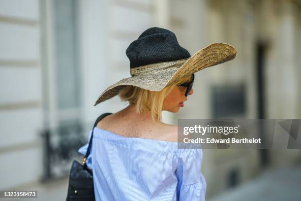 Emy Venturini wears a beige and black wicker large hat from Reinhard Plank, black sunglasses, a gold necklace, a pale blue and white stripes...