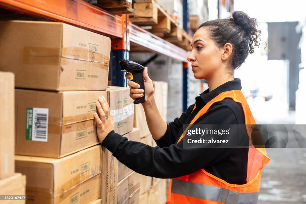 Woman scanning boxes with bar code scanner in warehouse shelf