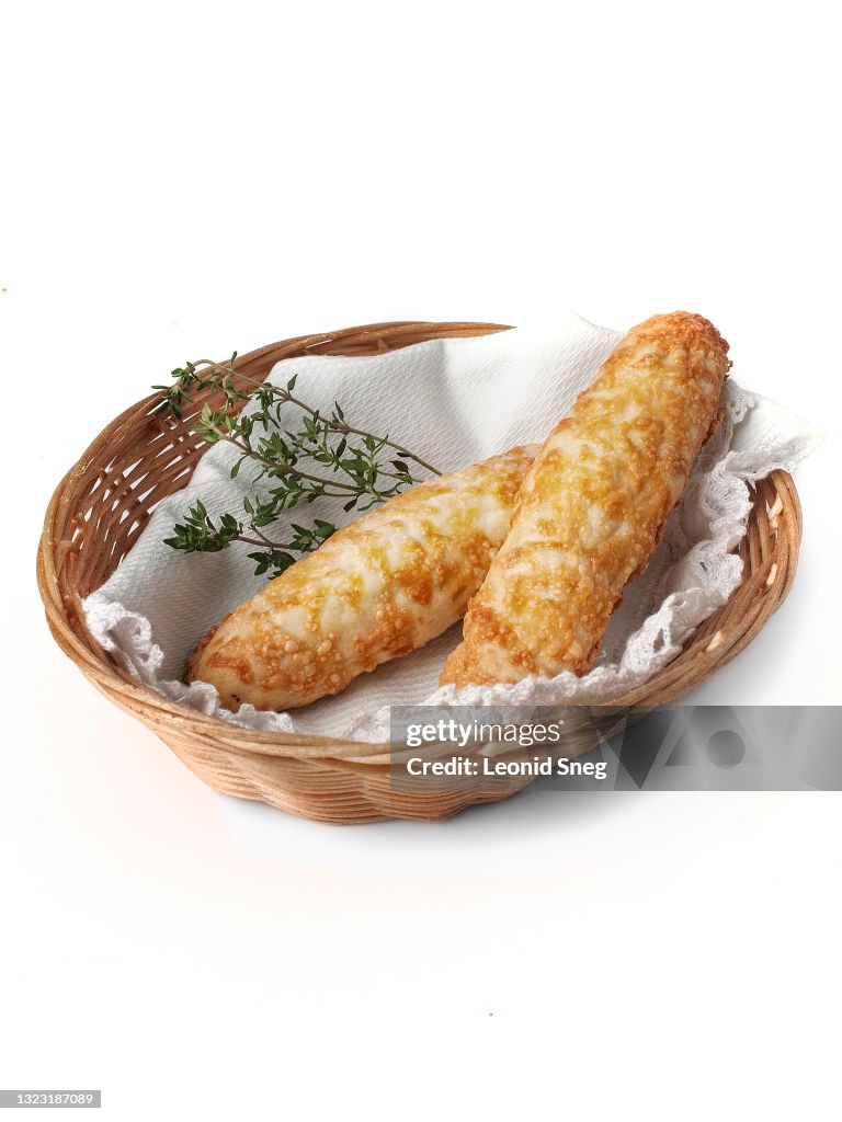 Food photography of homemade buns, bread and cheese sticks (breadsticks with cheese) made from yeast dough side view in a wicker straw basket on a white background isolated close up