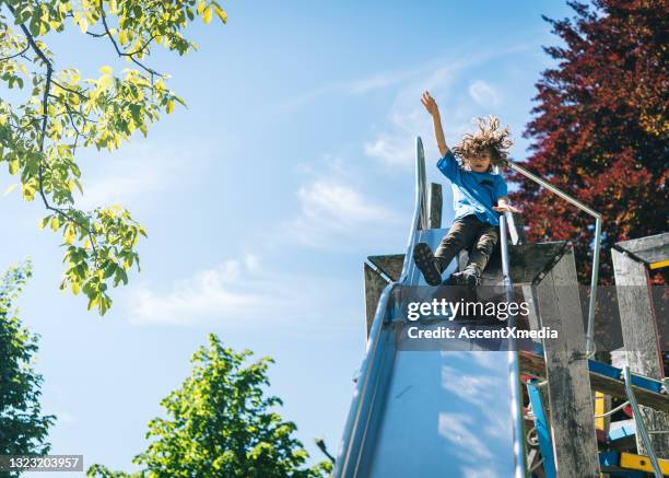 junge rutscht rutsche auf spielplatz - rutsche stock-fotos und bilder
