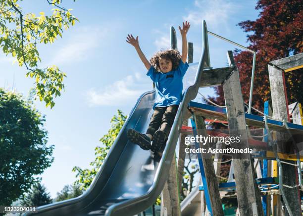 junge rutscht rutsche auf spielplatz - kinderspielplatz stock-fotos und bilder