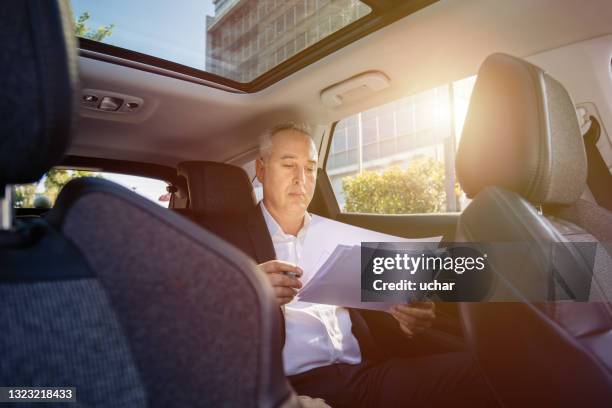 rich businessman sitting in backseat of vehicle and examining documents - luxury hotel room stock pictures, royalty-free photos & images