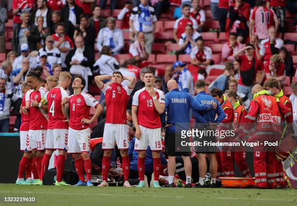Thomas Delaney, Andreas Christensen and Jonas Wind of Denmark look dejected as Christian Eriksen of Denmark receives medical treatment during the...