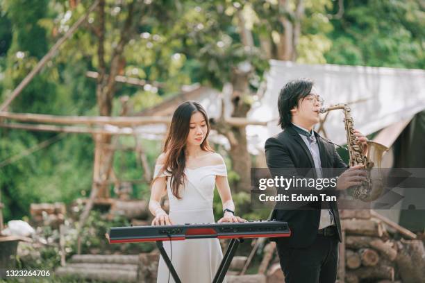 asian chinese couple saxophonist keyboard player band performing practicing at rural area with formal wear - electric piano stock pictures, royalty-free photos & images