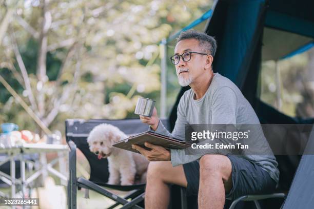 asian chinese senior man using digital tablet at camping chair in the morning with his toy poodle companion - dog camping stock pictures, royalty-free photos & images