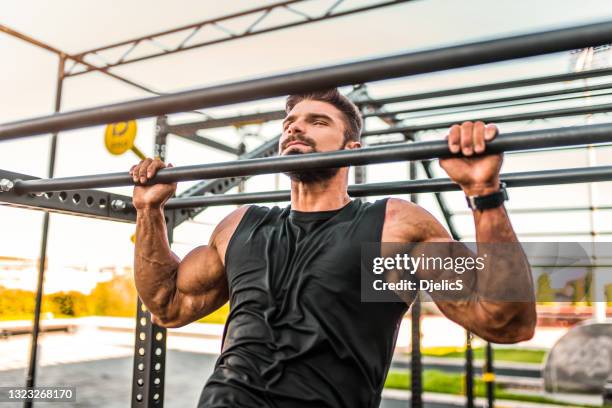 young bodybuilder doing pullups at the outdoor gym. - pull ups stock pictures, royalty-free photos & images