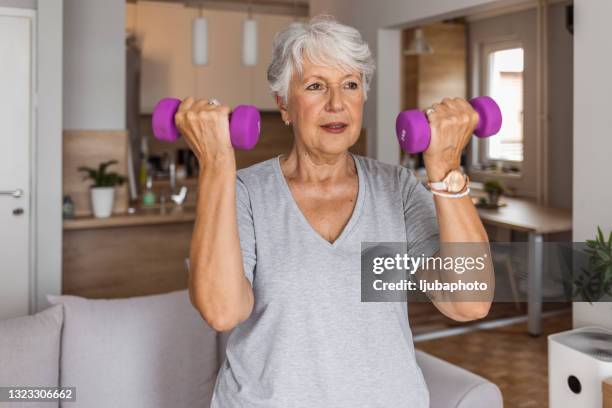 smiling senior woman lifting dumbbells while working out at home - weight lifting imagens e fotografias de stock