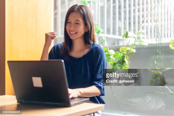 susseccful businesswoman celebrating at her desk in home office - bid stock pictures, royalty-free photos & images