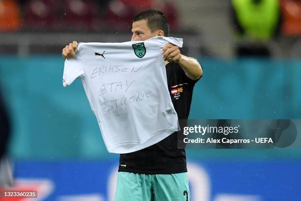 Stefan Lainer of Austria celebrates after scoring their side's first goal whilst holding a t-shirt with a message of support for Christian Eriksen of...