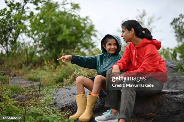 mother and daughter sitting on the rock and enjoying rain - indian mother stockfoto's en -beelden