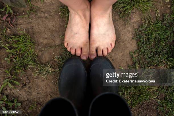 the child's bare feet on the ground. opposite are black rubber boots. - pair stock photos et images de collection