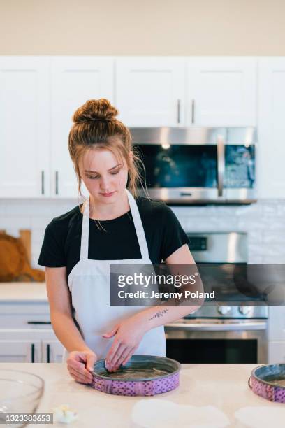 young woman greasing pans while baking a delicious chocolate cake at home - messy hair bun stock pictures, royalty-free photos & images