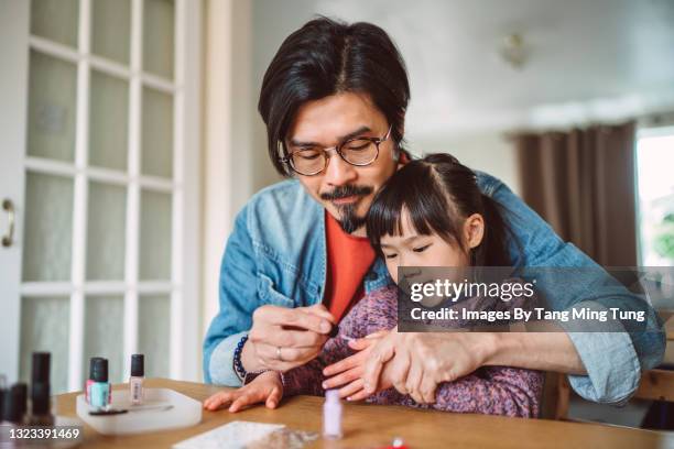 young handsome dad polishing his daughter’s fingernails at home joyfully - single father stockfoto's en -beelden